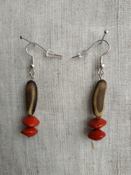 Boucles d'oreilles en gros plan sur fond gris. Chaque boucle contient 2 graines l'église et un flamboyant